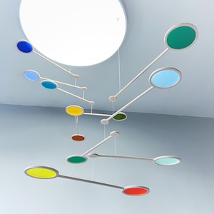 May include: A colourful mobile with round discs in various colours, including blue, green, yellow, orange, and red, hanging from a white ceiling.