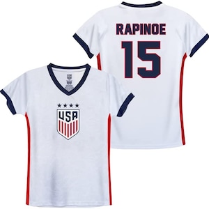 May include: White soccer jersey with red and blue trim. The jersey has the USA logo on the front and the name "RAPINOE" and the number "15" on the back.