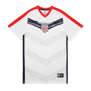 May include: White soccer jersey with red and navy blue accents. The jersey features a stylized brushstroke design and the word "USA" in a navy blue shield.