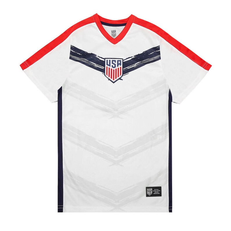 May include: White soccer jersey with red and navy blue accents. The jersey features a stylized brushstroke design and the word "USA" in a navy blue shield.