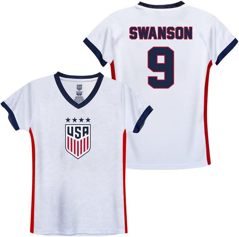 Puede incluir: Camiseta de f&uacute;tbol blanca con ribetes rojos y azules. La camiseta tiene el logotipo de EE. UU. en la parte delantera y el nombre "SWANSON" y el n&uacute;mero "9" en la parte posterior.