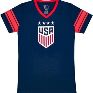 May include: A navy blue t-shirt with red and white stripes on the sleeves. The shirt has a v-neck and features a white shield with the word "USA" and five stars above it.