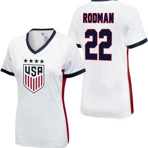 K&ouml;nnte beinhalten: Wei&szlig;es Fu&szlig;balltrikot mit roten und blauen Akzenten. Das Trikot hat das USA-Logo auf der Vorderseite und den Namen "Rodman" sowie die Nummer "22" auf der R&uuml;ckseite.