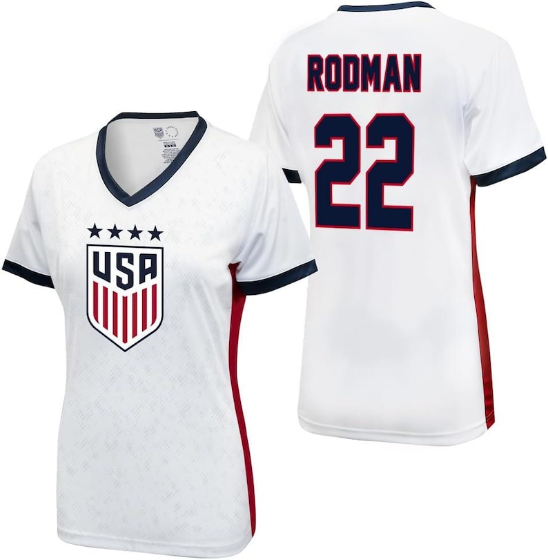 K&ouml;nnte beinhalten: Wei&szlig;es Fu&szlig;balltrikot mit roten und blauen Akzenten. Das Trikot hat das USA-Logo auf der Vorderseite und den Namen "Rodman" sowie die Nummer "22" auf der R&uuml;ckseite.