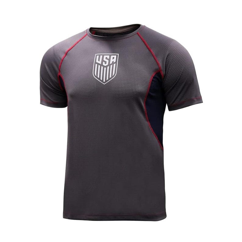 May include: Dark gray athletic t-shirt with short sleeves. Features a white shield logo with the letters "USA" and red stitching along the seams. The shirt has a navy blue panel on the side and is made of a breathable, textured fabric.