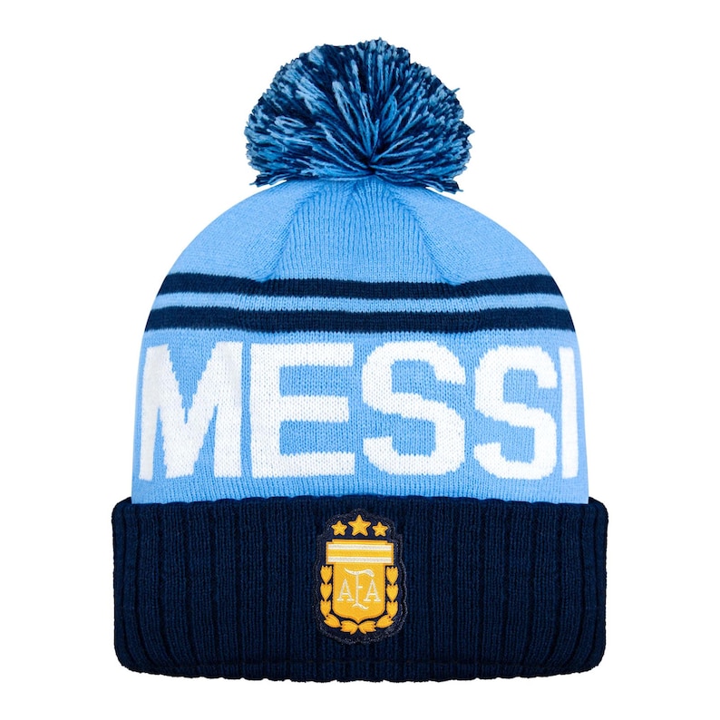 Puede incluir: Un gorro de punto azul claro y azul marino con pomp&oacute;n. La palabra "MESSI" se muestra en letras blancas en la parte delantera. La banda inferior presenta un parche con un emblema dorado y tres estrellas.