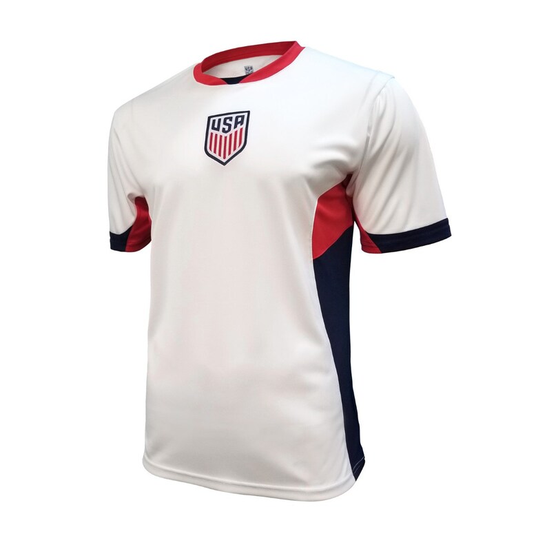 Puede incluir: Camiseta de f&uacute;tbol blanca con un logotipo de EE. UU. rojo, blanco y azul en la parte delantera. La camiseta tiene detalles en azul marino y rojo en las mangas.