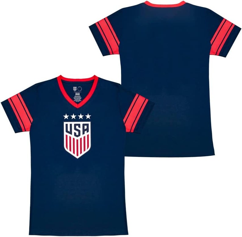 Puede incluir: Camiseta azul marino con ribetes rojos y blancos en las mangas. La camiseta presenta un escudo blanco con estrellas y la palabra "USA" en el centro.
