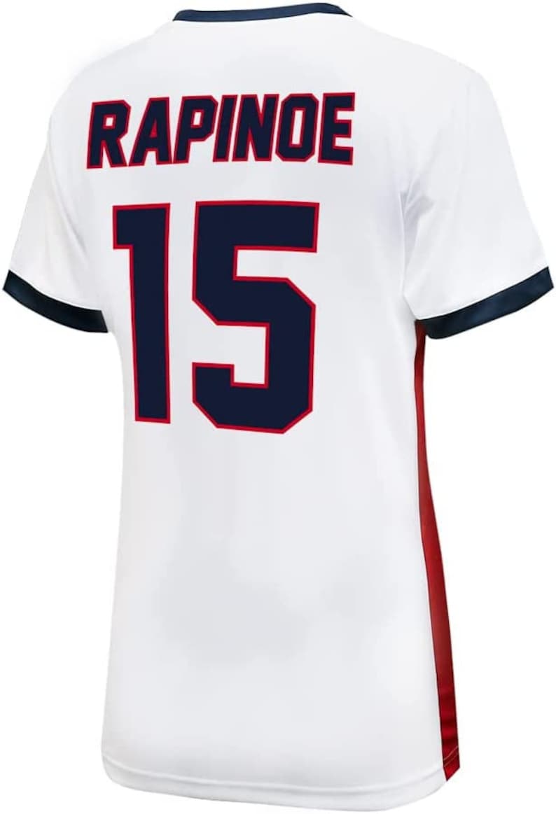 May include: White soccer jersey with blue and red trim. The back of the jersey has the name "RAPINOE" and the number "15" in blue.