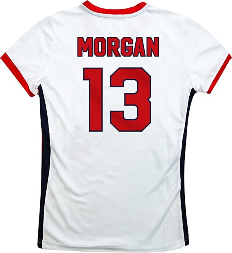 May include: White soccer jersey with red and blue trim. The back of the jersey has the name "MORGAN" and the number "13" in red with a blue outline.