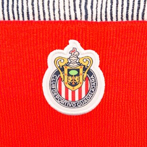 Puede incluir: Primer plano de una tela roja de punto con un borde a rayas blanco y azul marino. Un parche circular con el logotipo del Club Deportivo Guadalajara est&aacute; centrado en la tela roja. El parche tiene un borde blanco e incluye el escudo y el texto del equipo.