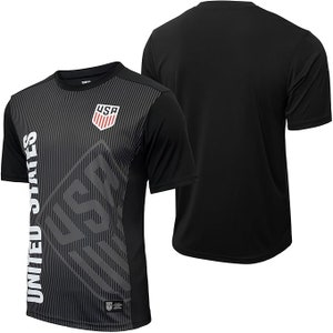Puede incluir: Camiseta de f&uacute;tbol negra con un dise&ntilde;o gr&aacute;fico gris y blanco con las palabras "United States" y "USA".