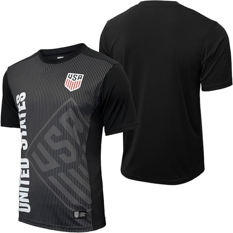 Puede incluir: Camiseta de f&uacute;tbol negra con un dise&ntilde;o gr&aacute;fico gris y blanco con las palabras "United States" y "USA".