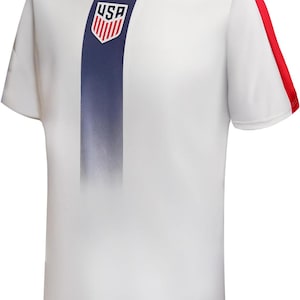 May include: White athletic t-shirt with a blue vertical stripe down the front, featuring the USA logo. Red accents are on the sleeves and collar. The shirt is short-sleeved.