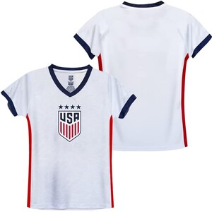 May include: White soccer jersey with red and navy blue trim. The jersey features the USA crest with five stars and the word "USA" in red.