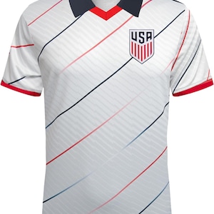 May include: White football shirt with diagonal red and blue stripes. The shirt features a navy blue collar with a red V-neck and red sleeve cuffs. The USA emblem is on the chest.