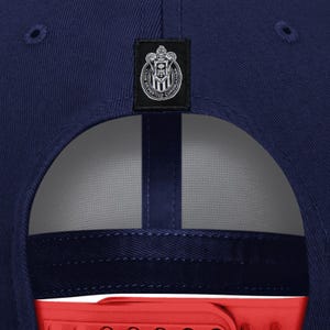 May include: A navy blue baseball cap with a red bill. The cap features a small, rectangular patch with a team logo and text. The logo is a crest with a shield and the words "CLUB DEPORTIVO GUADALAJARA".