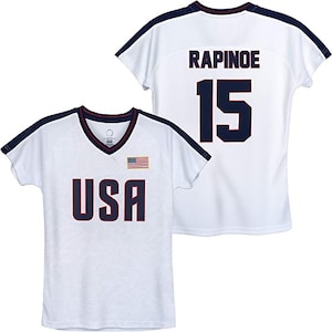 K&ouml;nnte beinhalten: Wei&szlig;es Fu&szlig;balltrikot mit blauen und roten Akzenten. Die Vorderseite des Trikots tr&auml;gt den Schriftzug "USA" in Blau mit einer kleinen amerikanischen Flagge. Die R&uuml;ckseite des Trikots tr&auml;gt den Namen "RAPINOE" und die Nummer "15" in Blau.