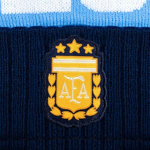Puede incluir: Un gorro de punto azul marino con una banda azul claro y blanca. El gorro presenta un parche con el emblema de la Asociaci&oacute;n del F&uacute;tbol Argentino, que incluye estrellas doradas, un escudo y las letras "AFA".