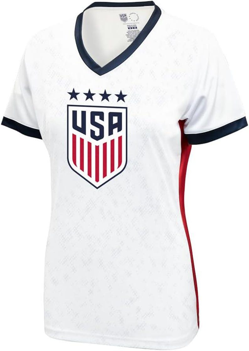 Pu&ograve; includere: Maglia da calcio bianca con uno stemma USA blu e rosso e cinque stelle. La maglia ha un colletto blu scuro e bordi sulle maniche. I lati della maglia hanno accenti rossi.