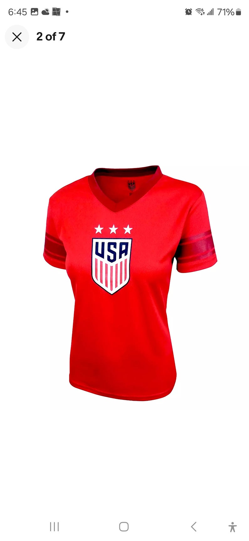Puede incluir: Camiseta de f&uacute;tbol roja de manga corta con un escudo azul y blanco de los Estados Unidos con tres estrellas sobre el escudo. La camiseta tiene rayas rojas en las mangas.
