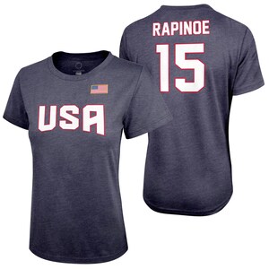Pode incluir: Uma camiseta azul marinho com a palavra "USA" impressa em branco na frente e o nome "RAPINOE" e o n&uacute;mero "15" impressos em branco nas costas.