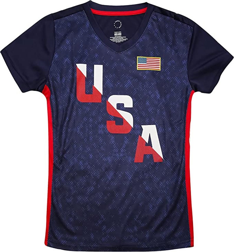 Pu&ograve; includere: Una maglietta blu navy con una grafica USA rosso, bianco e blu e una piccola bandiera americana sul petto. La maglietta ha pannelli laterali rossi e un collo a V.