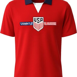 Puede incluir: Camiseta de f&uacute;tbol roja de manga corta con cuello azul marino y cuello en V blanco. La camiseta presenta el texto "USMNT" y "U.S. Soccer Federation" con un logotipo de escudo de EE. UU.