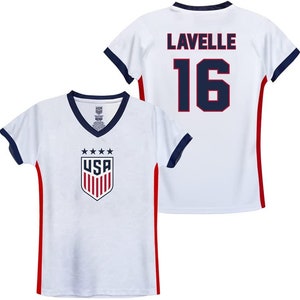 Op de afbeelding: Wit voetbaltenue met rode en blauwe bies. Het tenue heeft het USA-logo op de voorkant en de naam "Lavelle" en het nummer "16" op de achterkant.