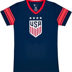 May include: A navy blue t-shirt with red and white stripes on the sleeves. The shirt has a white v-neck and a white USA logo with five stars and red and white stripes.