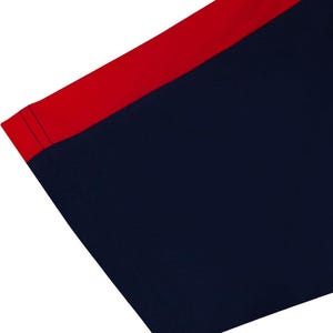 May include: Close-up of a navy blue garment with a red accent. The red accent is a stripe along the top edge. The navy blue fabric is smooth and appears to be a knit material. The edges are neatly sewn with a dark blue thread.