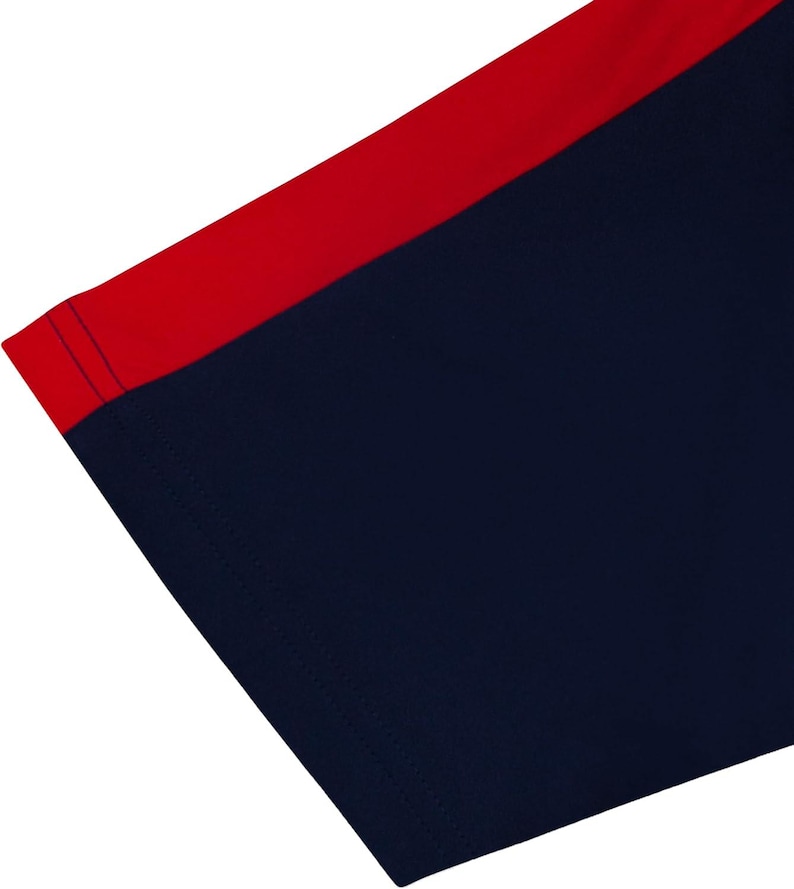 May include: Close-up of a navy blue garment with a red accent. The red accent is a stripe along the top edge. The navy blue fabric is smooth and appears to be a knit material. The edges are neatly sewn with a dark blue thread.