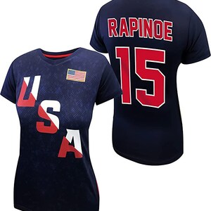 May include: A navy blue t-shirt with the text "USA" printed in red, white, and blue on the front and the text "RAPINOE 15" printed in red on the back.