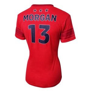 K&ouml;nnte beinhalten: Rotes Fu&szlig;balltrikot mit blauen Sternen und Streifen. Auf der R&uuml;ckseite des Trikots sind der Name "MORGAN" und die Nummer "13" in Blau gedruckt.