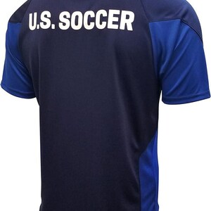 Puede incluir: Una camiseta de f&uacute;tbol azul marino con detalles en azul y blanco. La parte posterior de la camiseta tiene el texto "U.S. SOCCER" impreso en blanco.