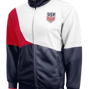 Puede incluir: Una chaqueta con cremallera blanca, roja y azul marino con un logotipo de EE. UU. en el pecho.
