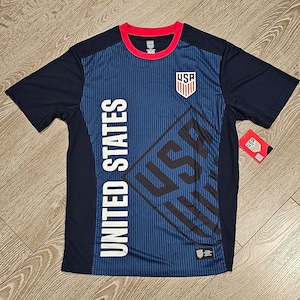 May include: A navy blue soccer jersey with a white "UNITED STATES" and "USA" graphic on the front. The jersey has a red and white trim around the neck and a red "USA" logo on the chest.