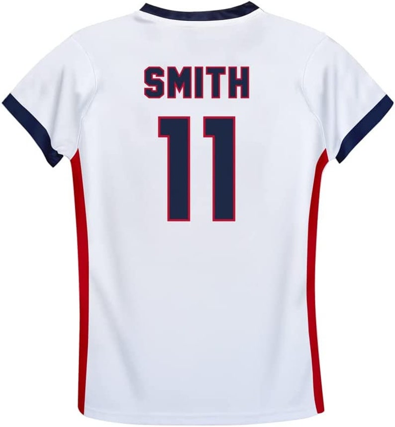May include: White athletic jersey with the name "SMITH" and the number "11" in navy blue. The jersey has navy blue trim on the sleeves and a red stripe down the sides.