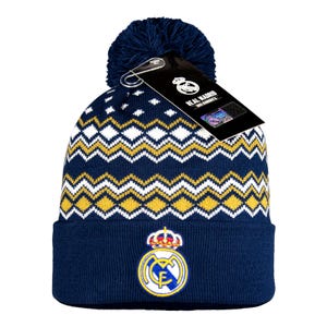 May include: Navy blue knit beanie with a pom-pom. The hat features a white and yellow zigzag pattern and a Real Madrid logo. A tag with the Real Madrid logo is attached to the hat.
