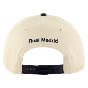 May include: A cream-colored baseball cap with the text "Real Madrid" in navy blue across the back. The cap has a navy blue button on top and a black adjustable strap.