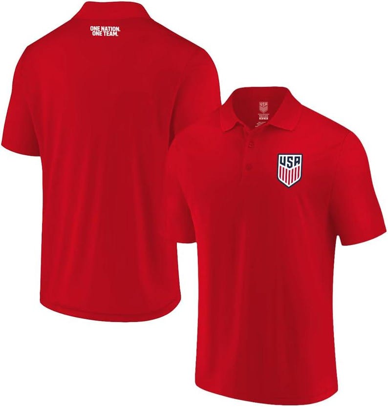 May include: A bright red short-sleeved polo shirt featuring a collar with a button placket. The front displays a USA shield logo in red, white, and blue. The back of the shirt includes the white text "ONE NATION. ONE TEAM." near the neckline.