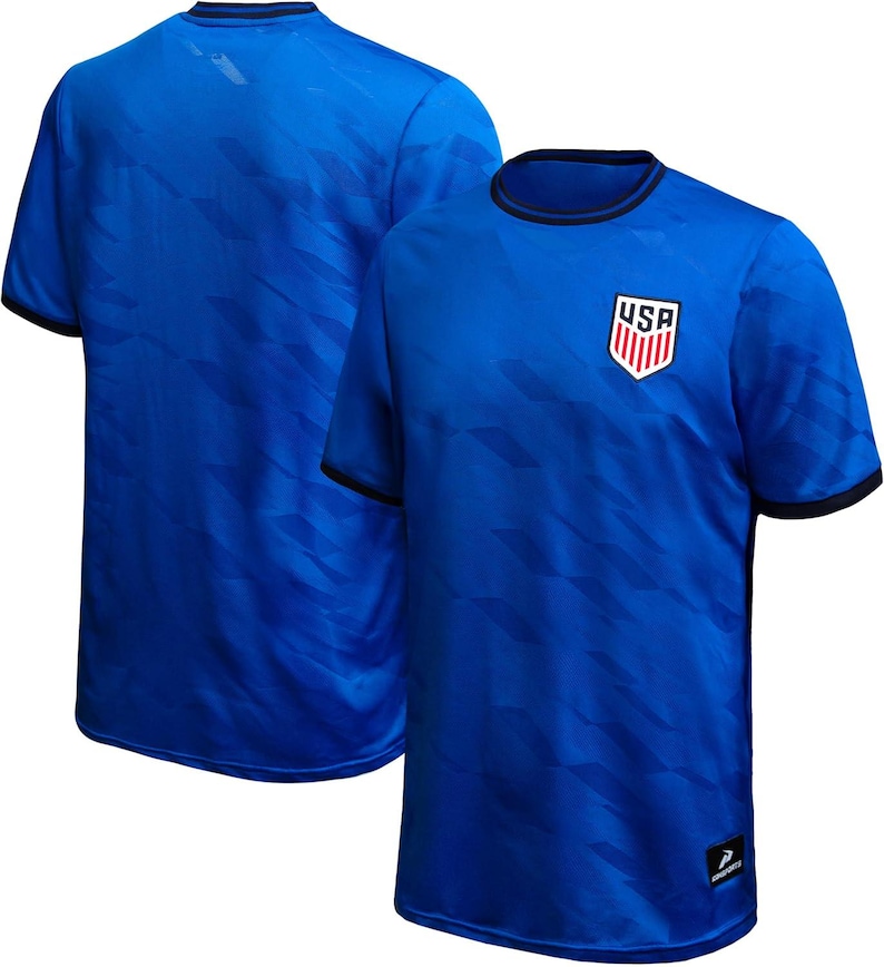 May include: Two blue soccer jerseys. The front jersey has a USA crest on the chest and black trim on the collar and sleeves. The jerseys have a subtle geometric pattern. The second jersey is in the background, showing the back of the shirt.