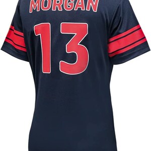 May include: Navy blue football shirt with red and white stripes on the sleeves. The back of the shirt has the name "MORGAN" and the number "13" in red.
