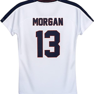 Peut inclure: Maillot de sport blanc avec le nom "MORGAN" et le num&eacute;ro "13" en bleu marine avec une bordure rouge. Le maillot a des accents bleu marine sur les &eacute;paules et l'encolure. Le dos du maillot est visible.
