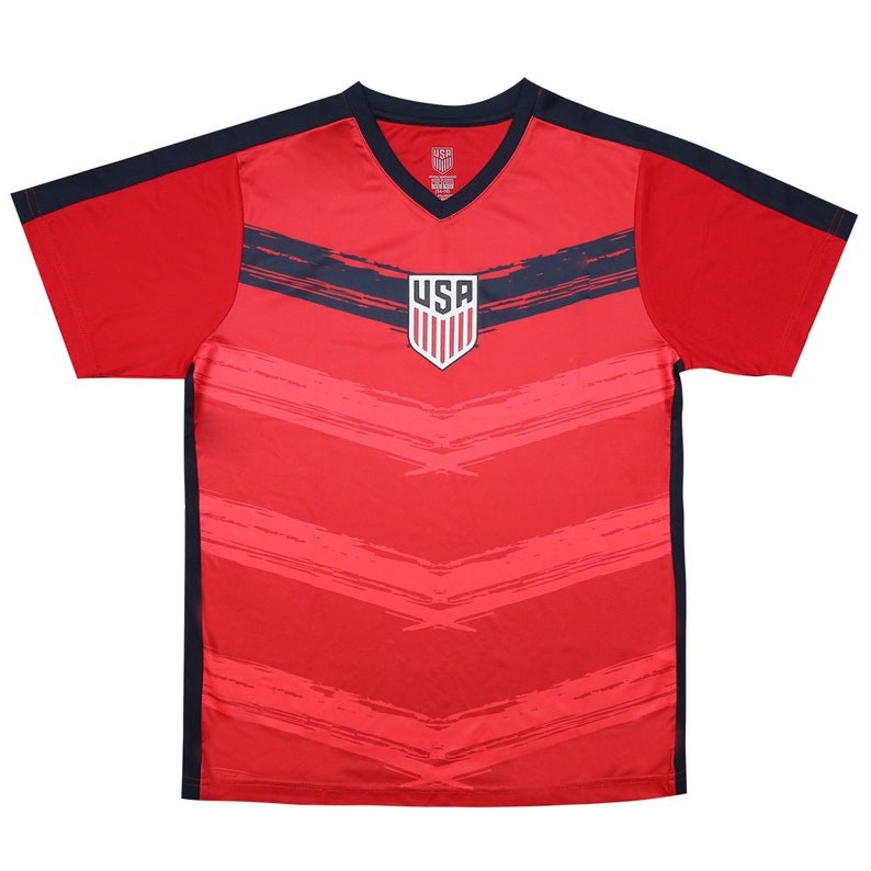 Op de afbeelding: Rood voetbaltenue met blauw-wit USA-logo en zwarte accenten. Het tenue heeft een V-hals en korte mouwen.