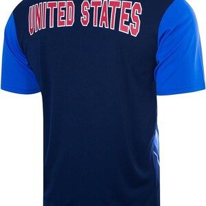 K&ouml;nnte beinhalten: Ein marineblaues T-Shirt mit kurzen &Auml;rmeln und einem royalblauen und wei&szlig;en Design auf der rechten Seite. Auf der R&uuml;ckseite des Shirts steht in Rot "UNITED STATES" gedruckt.