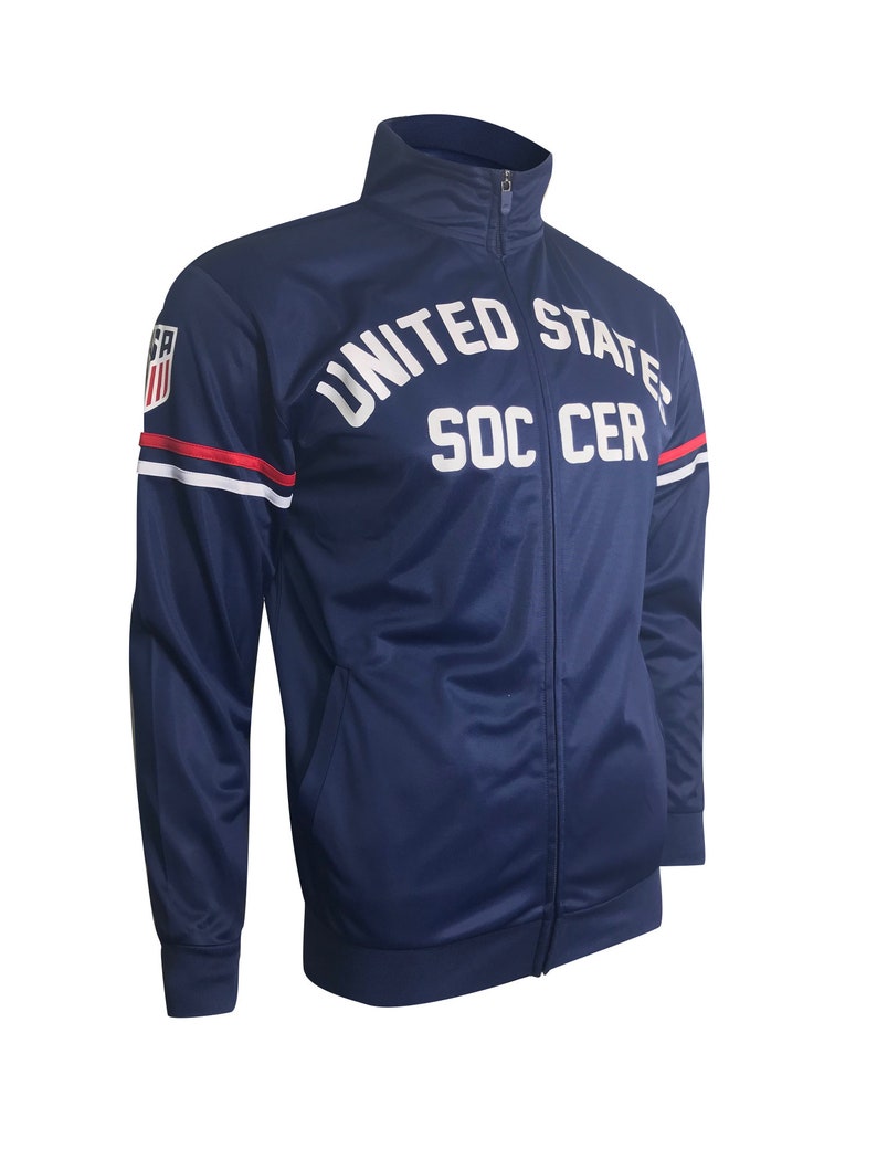 May include: A navy blue zip-up jacket with white accents and the words "UNITED STATES SOCCER" printed on the front.