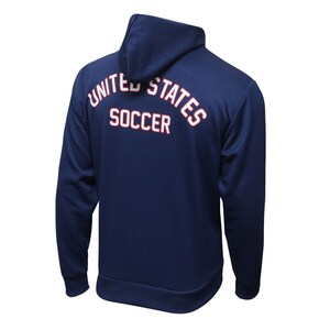 以下が含まれることがあります： 背面に「UNITED STATES SOCCER」の文字が白で書かれ、赤色のアウトラインが描かれたネイビーブルーのフード付きスウェットシャツです。