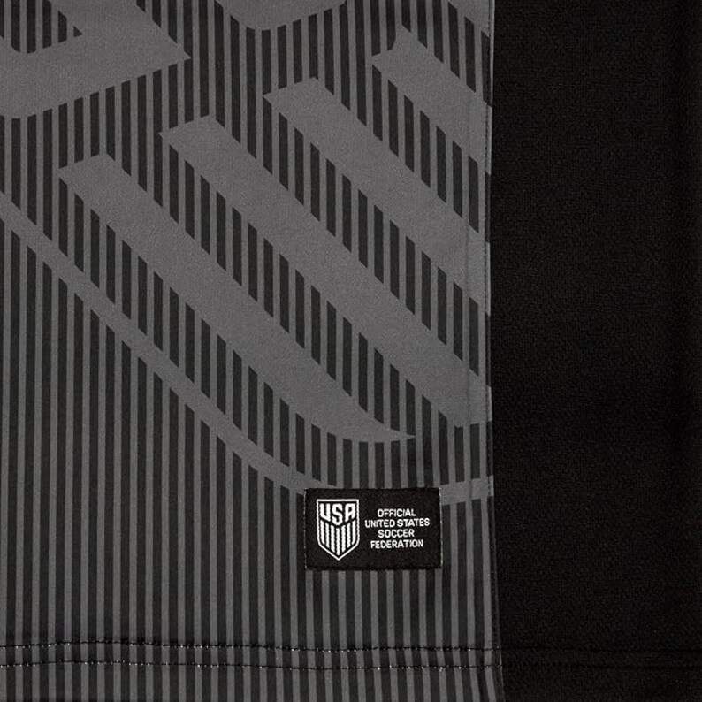 May include: A black and gray soccer jersey with a geometric pattern. The jersey has a patch on the front that says "Official United States Soccer Federation".