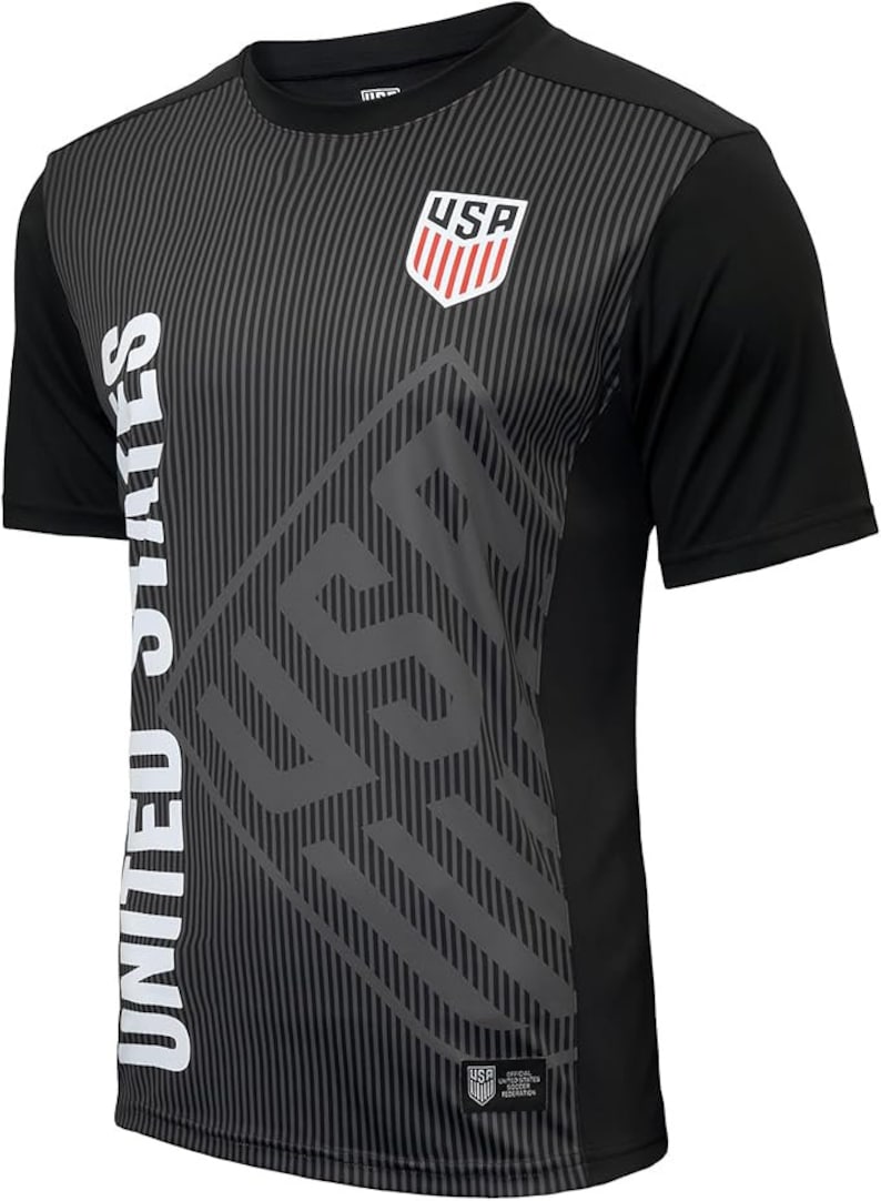 May include: Black short-sleeved soccer jersey with a gray and white graphic design. The graphic features the words "USA" and "UNITED STATES" and a shield with the letters "USA" inside.